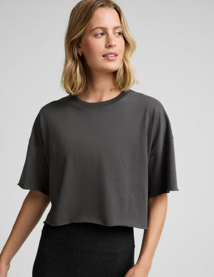 Woman wearing a dark gray cropped t-shirt and black leggings against a plain background. 