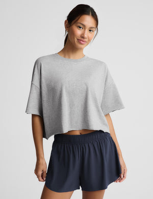 A woman modeling a light gray cropped short-sleeve t-shirt and navy blue athletic shorts against a light gray studio background.