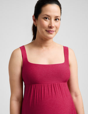 Pregnant woman wearing a red dress against a plain background. 