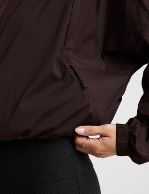 Woman wearing a brown jacket and black leggings against a plain background. 