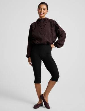 Woman wearing a brown jacket and black leggings against a plain background. 