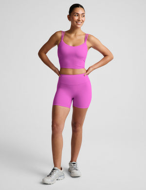 Woman wearing a purple cropped tank and purple biker shorts against a plain background. 