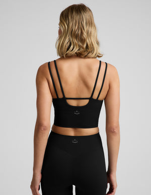Woman wearing a black cropped strappy tank top and biker shorts against a plain background. 