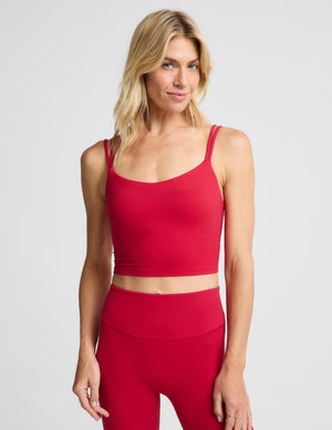 A woman modeling a matching red activewear set consisting of a scoop-neck crop top and high-waisted leggings, photographed against a solid light gray background.