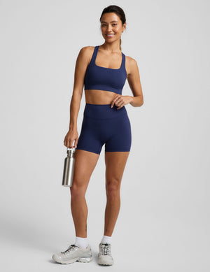 Woman wearing a blue sports bra and blue biker shorts against a plain background. 