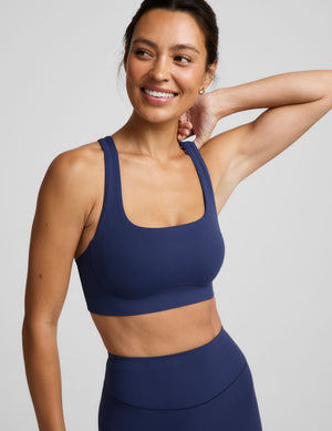 Woman wearing a blue sports bra and blue biker shorts against a plain background. 