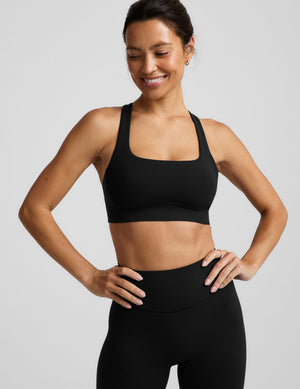 A woman in a black sports bra and black midi length leggings against a plain background. 