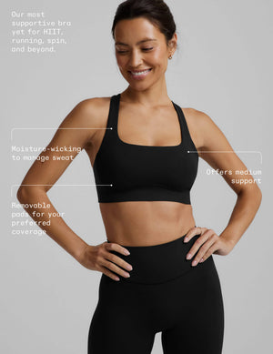 A woman in a black sports bra and black midi length leggings against a plain background with text product callouts on top. 