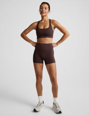 Woman wearing a brown sports bra and brown biker shorts against a plain background. 