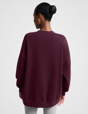A woman modeling an oversized crewneck sweatshirt in deep burgundy, paired with light gray leggings, against a solid light gray background.