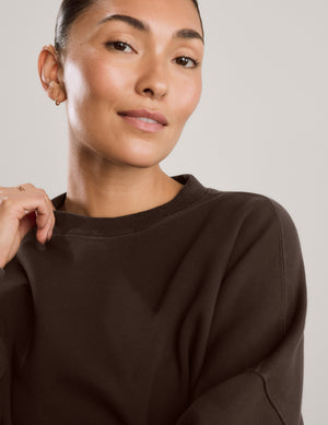 Woman wearing a brown oversized crewneck sweatshirt and black leggings against a plain background. 