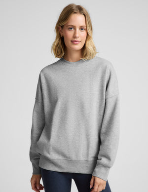 Woman wearing a gray oversized crewneck sweatshirt and navy blue leggings against a plain background. 
