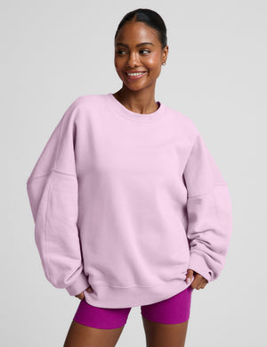 Woman wearing a light purple oversized crewneck sweatshirt and purple biker shorts against a plain background. 