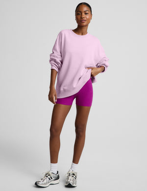 Woman wearing a light purple oversized crewneck sweatshirt and purple biker shorts against a plain background. 