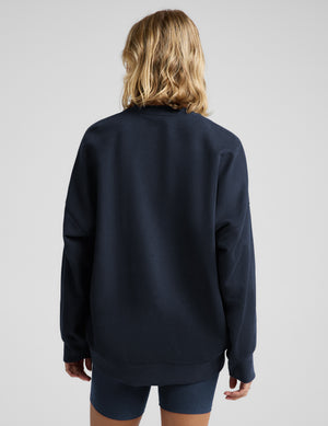 Woman wearing a navy blue oversized crewneck sweatshirt and biker shorts against a plain background. 