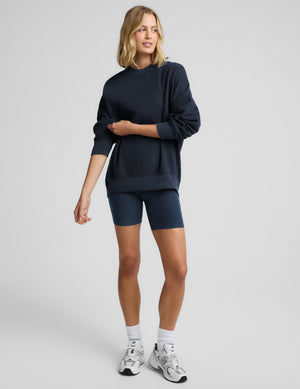 Woman wearing a navy blue oversized crewneck sweatshirt and biker shorts against a plain background. 