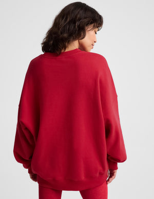A woman wearing an oversized red crewneck sweatshirt and matching red leggings, photographed against a clean light gray studio background.