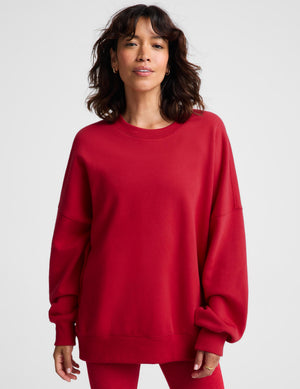 A woman wearing an oversized red crewneck sweatshirt and matching red leggings, photographed against a clean light gray studio background.