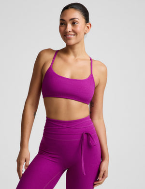 Woman wearing a purple bra and leggings against a plain background. 
