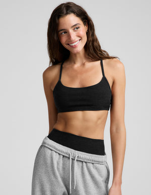 Woman wearing a black bra and gray sweatpants against a plain background. 