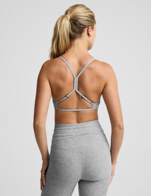 A woman modeling a light heather gray sports bra and matching high-waisted leggings with a drawstring waist, photographed against a solid light gray studio background.