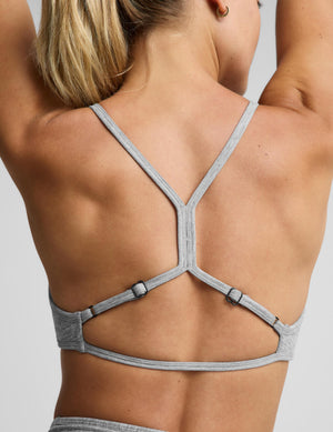 A woman modeling a light heather gray sports bra and matching high-waisted leggings with a drawstring waist, photographed against a solid light gray studio background.