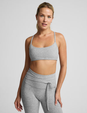 A woman modeling a light heather gray sports bra and matching high-waisted leggings with a drawstring waist, photographed against a solid light gray studio background.