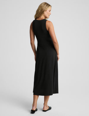 A woman modeling a sleeveless black midi dress from the back, standing against a light gray studio background.