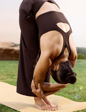 Woman wearing a brown cropped tank and brown athletic pants stretching. 