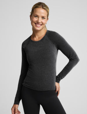 A woman modeling a dark heather gray long-sleeve athletic top with black leggings against a light gray studio background.