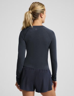 A woman shown from the back wearing a dark navy long-sleeve athletic top and matching shorts against a light gray studio background.