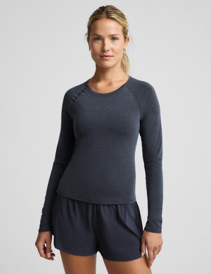 A woman modeling a dark slate blue long-sleeve athletic top with matching dark blue shorts against a light gray studio background.