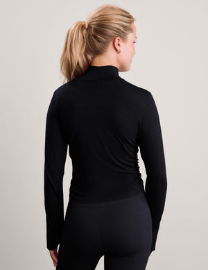 Woman wearing a black long sleeve turtle-neck paired with black leggings against a plain studio background. 