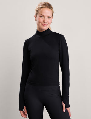 Woman wearing a black long sleeve turtle-neck paired with black leggings against a plain studio background. 