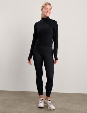 Woman wearing a black long sleeve turtle-neck paired with black leggings against a plain studio background. 