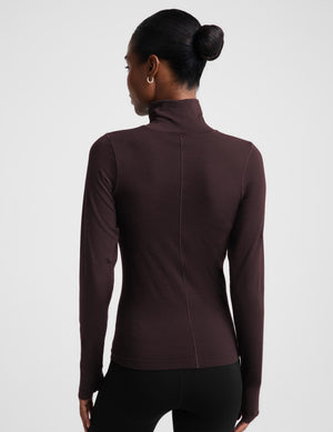 A woman modeling a dark brown long-sleeve turtle neck top and black pants against a light gray studio background.