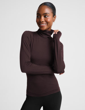 A woman modeling a dark brown long-sleeve turtle neck top and black pants against a light gray studio background.