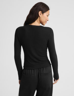 A woman shown from the back wearing a fitted black long-sleeve top and black pants against a light gray studio background.