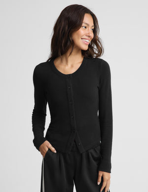 A woman wearing a black long-sleeve button-front cardigan top and black pants, photographed against a light gray studio background.