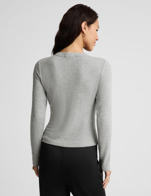 A woman shown from the back wearing a fitted light gray long-sleeve top and black pants against a plain light gray studio background.