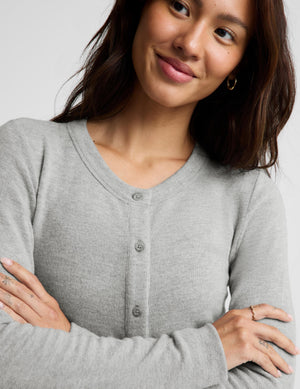 A woman wearing a light gray long-sleeve button-front cardigan sweater, shown from the chest up against a plain light gray studio background.