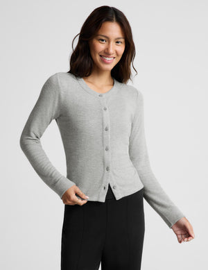 A woman modeling a light gray long-sleeve button-front cardigan sweater with black pants, photographed against a clean light gray studio background.