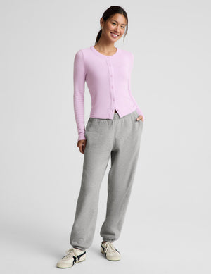 A woman modeling a light pink long-sleeve button-front top and heather gray sweatpants against a plain light gray studio background.