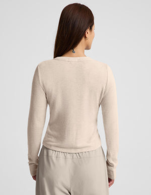 A woman modeling a light beige cropped button-front cardigan with long sleeves, paired with matching drawstring pants, against a plain light gray studio background.