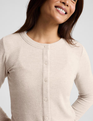 A woman modeling a light beige cropped button-front cardigan with long sleeves, paired with matching drawstring pants, against a plain light gray studio background.