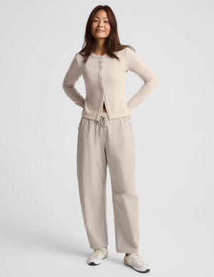 A woman modeling a light beige cropped button-front cardigan with long sleeves, paired with matching drawstring pants, against a plain light gray studio background.