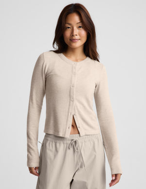 A woman modeling a light beige cropped button-front cardigan with long sleeves, paired with matching drawstring pants, against a plain light gray studio background.