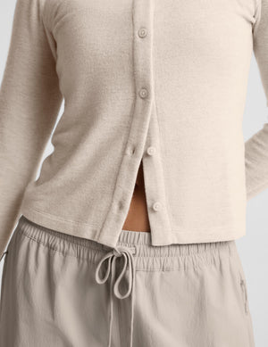 A woman modeling a light beige cropped button-front cardigan with long sleeves, paired with matching drawstring pants, against a plain light gray studio background.