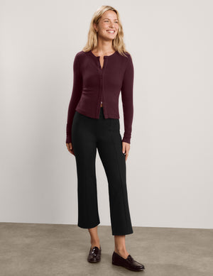 A woman wearing a long-sleeve button-front cardigan in deep burgundy, paired with black pants, photographed against a plain light gray studio background.