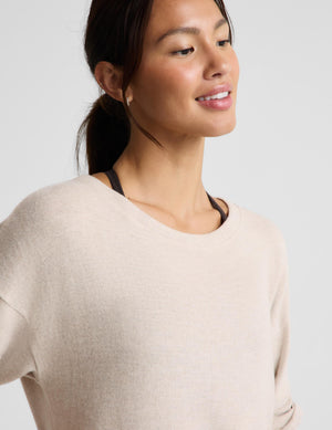 A woman wearing a light beige crewneck sweater, shown in a close-up profile view against a solid light gray background.
